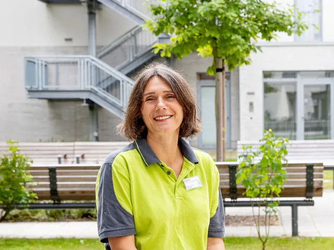 Mitarbeiterin bei PFLEGEN & WOHNEN MARIENTHAL Aida Bahic, vor der modernen und grünen Fassade am Standort.